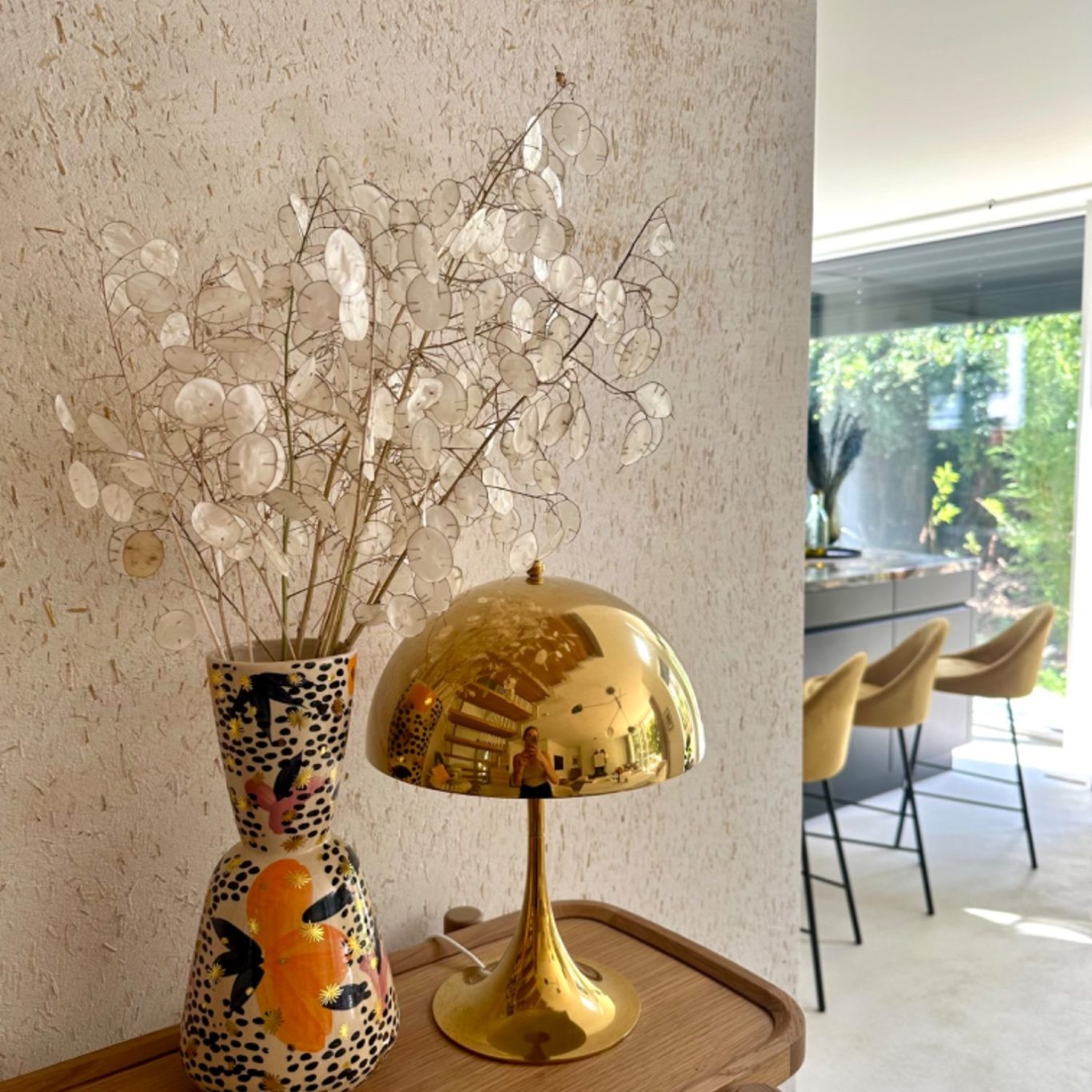 Vase mit Trockenblumen und goldener Lampe auf einem Holztisch in modernem Raum.